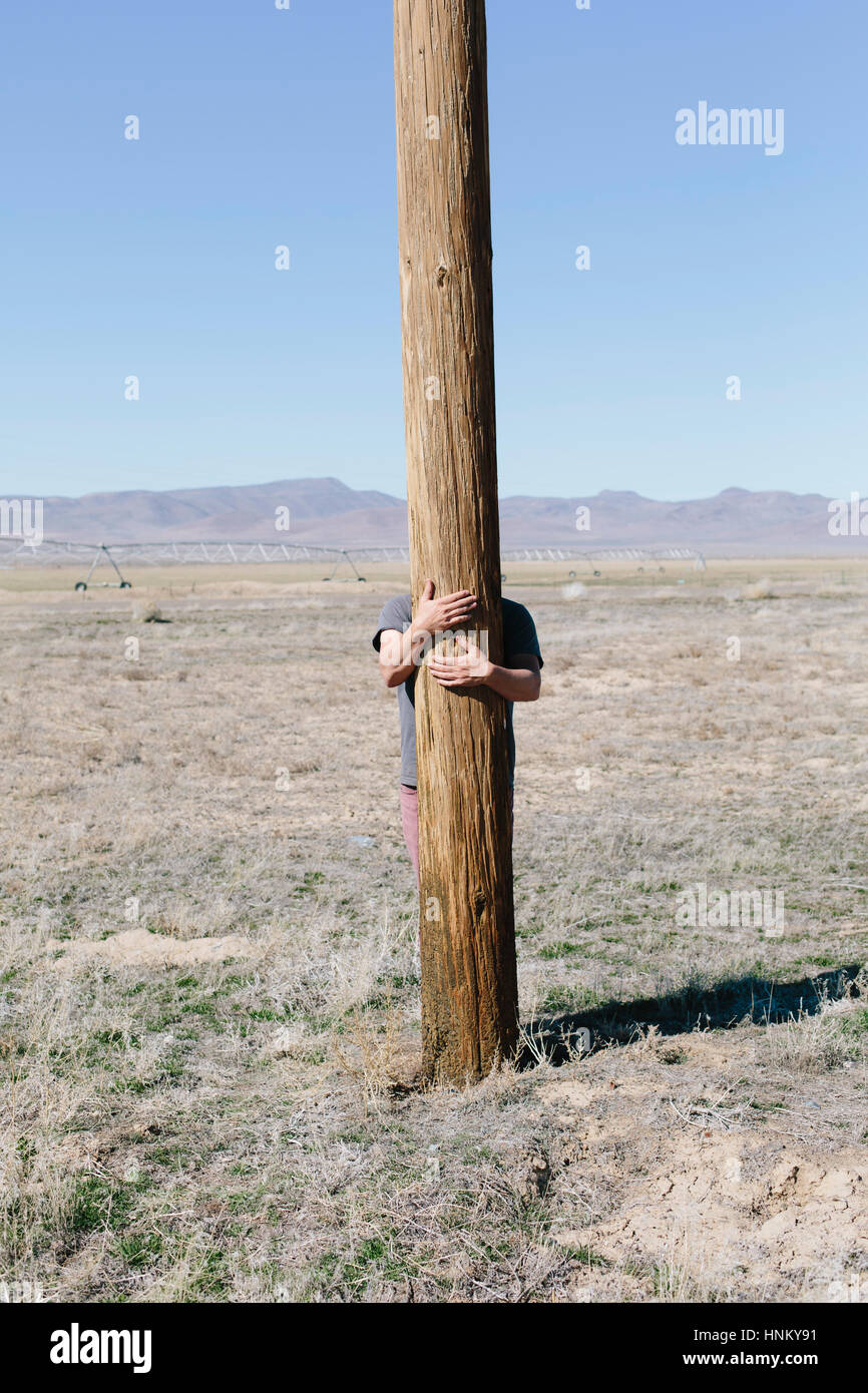 L'homme avec ses bras autour d'un poteau en bois utliities, accroché à l'étreindre ou poster dans un paysage ouvert. Banque D'Images