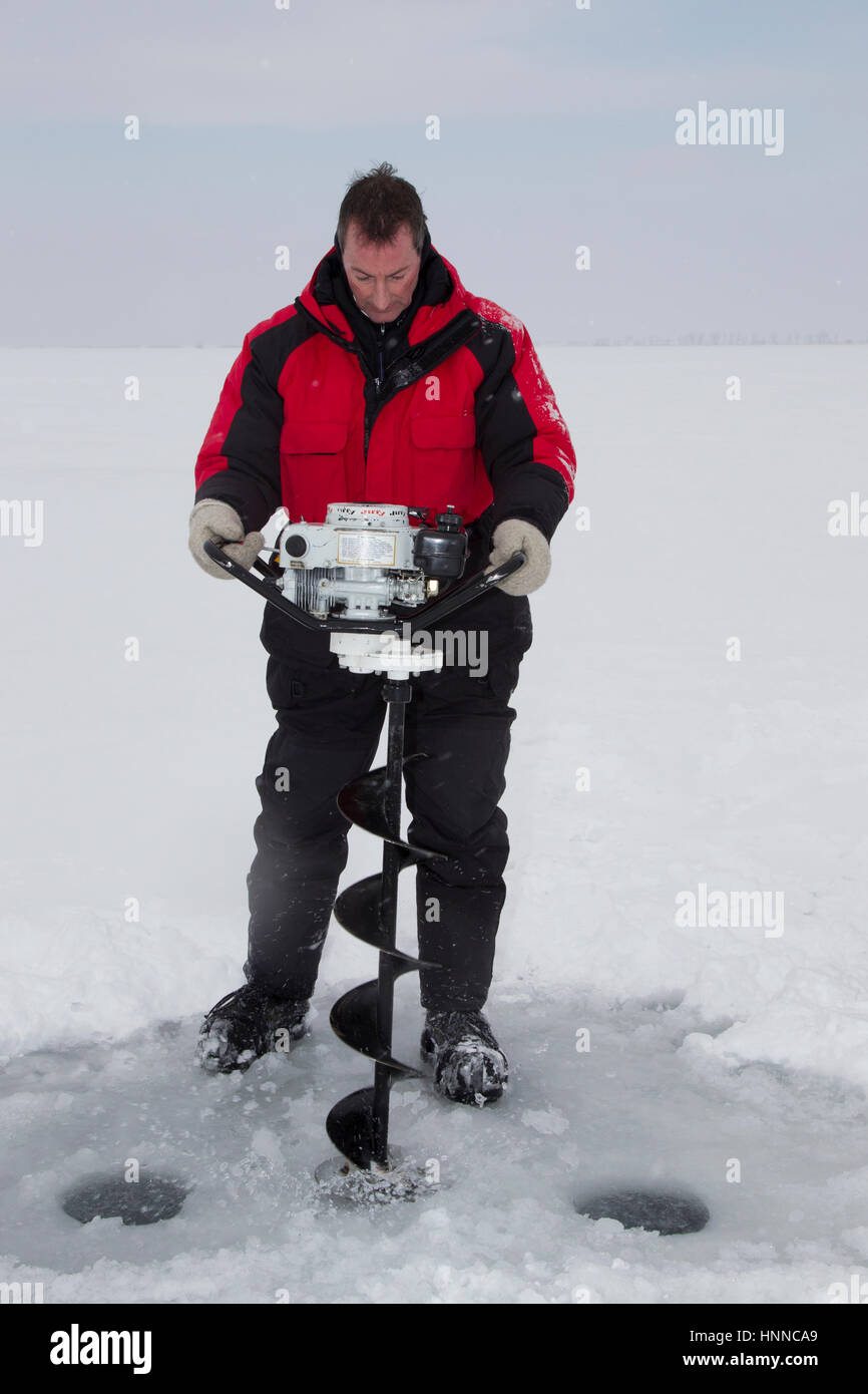 L'eau et pulvériser la caisse noire autour de ses bottes comme Doug Rohlf tire sa puissance de la vis d'un trou juste percés dans la glace de lac Frances, MT. (MR) Banque D'Images