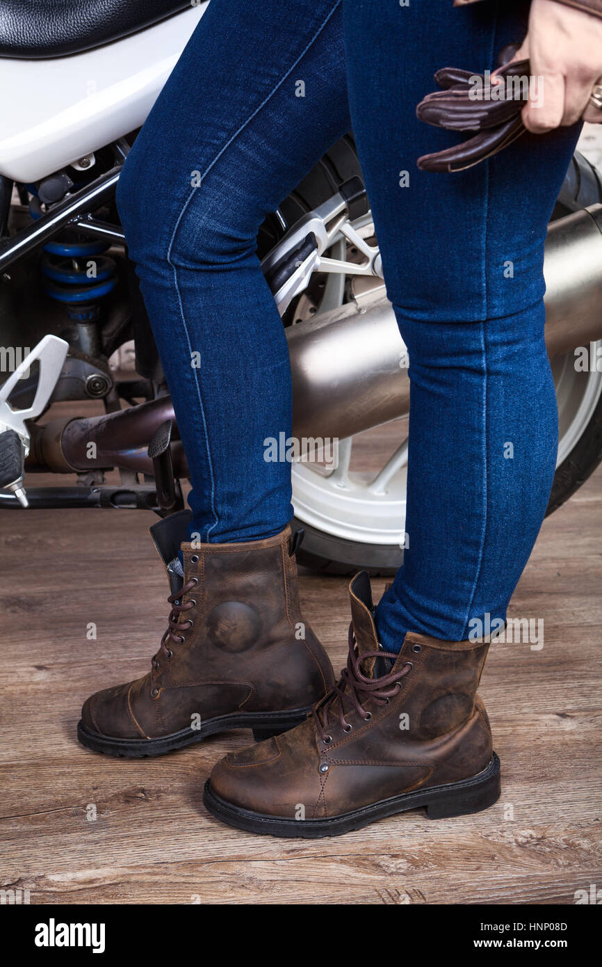 Les jambes des femmes porter un jean bleu et des chaussures de sécurité en cuir brun pour la moto sont près de moto, vue en gros Banque D'Images