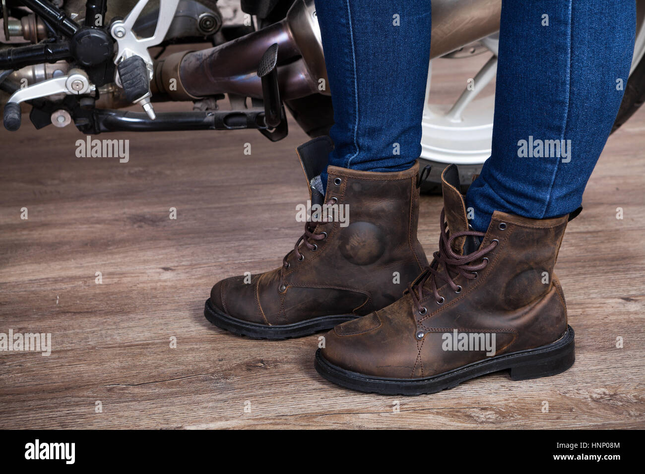 Demi-bottes en cuir brun pour la moto, les jambes dans le jeans est près de moto, vue en gros Banque D'Images
