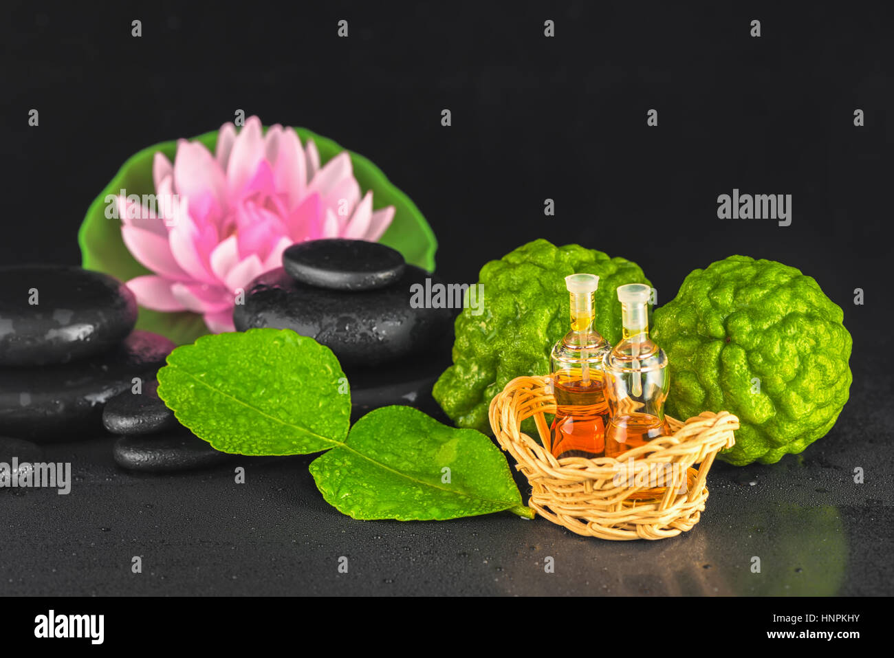 Spa concept de bergamote, Feuille, huile de parfum, lotus et des pierres de basalte zen avec de l'eau de la rosée sur fond noir, Close up Banque D'Images