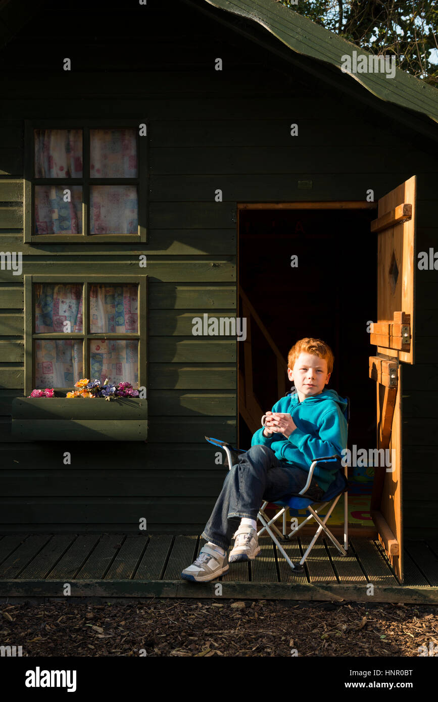 9 ans garçon assis en face de son jardin play house Banque D'Images