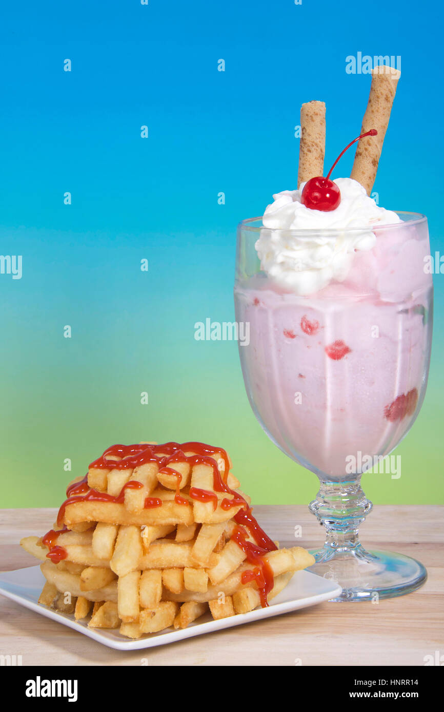 Salé et sucré. Frites empilés Criss Crossed sur une plaque carrée à côté d'une glace à la fraise dimanche avec de la crème fouettée, de cerise et de pirouette Banque D'Images
