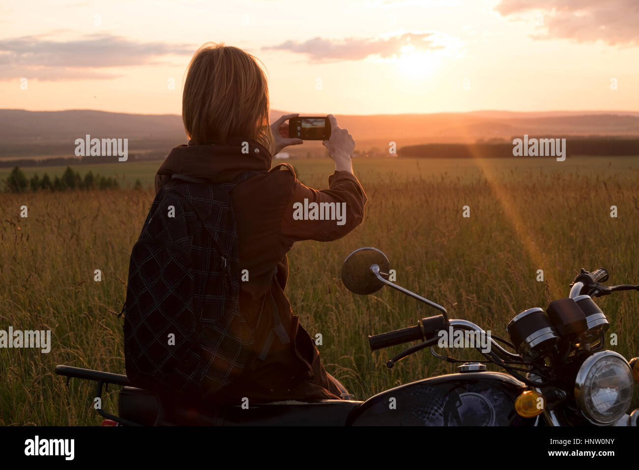 Caucasian woman avec moto dans domaine photographier le coucher du soleil Banque D'Images