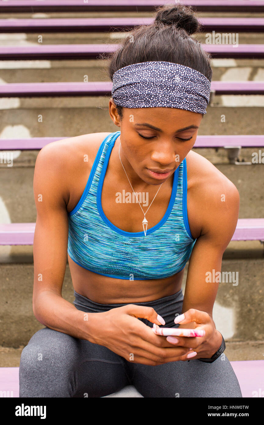 Femme noir assis sur des gradins texting on cell phone Banque D'Images