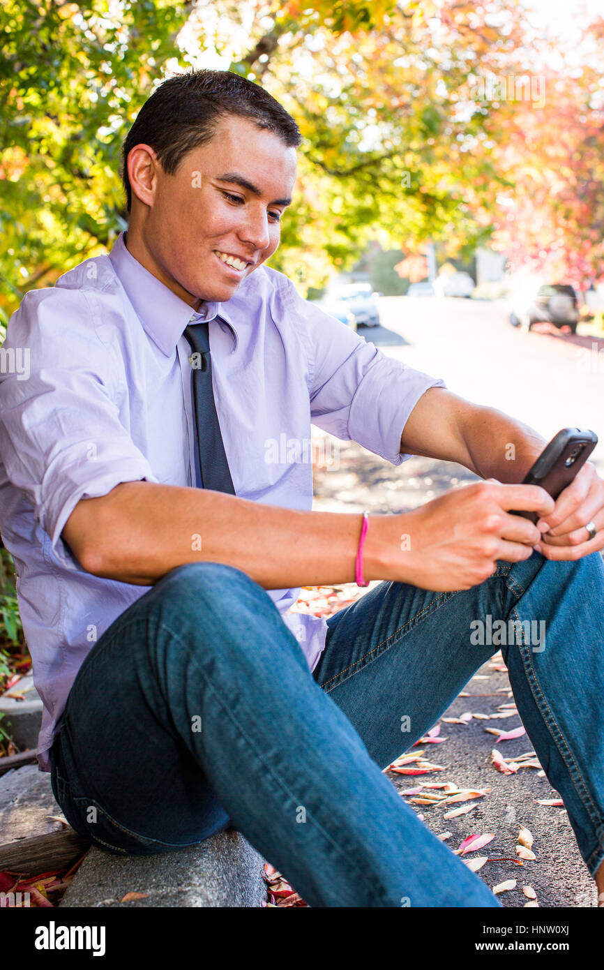 Smiling Mixed Race man sitting on curb texting on cell phone Banque D'Images