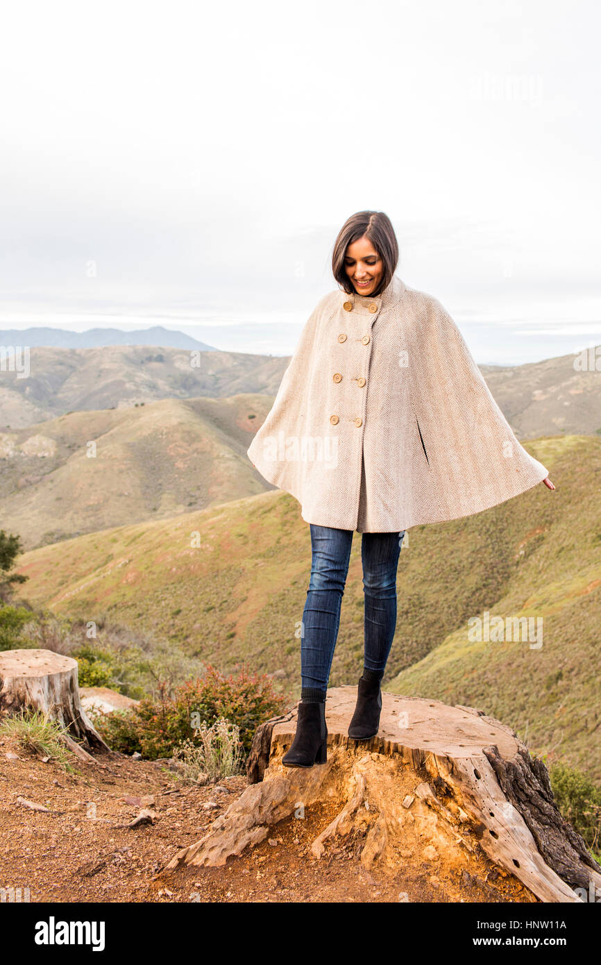 Smiling woman wearing poncho standing on tree stump Banque D'Images