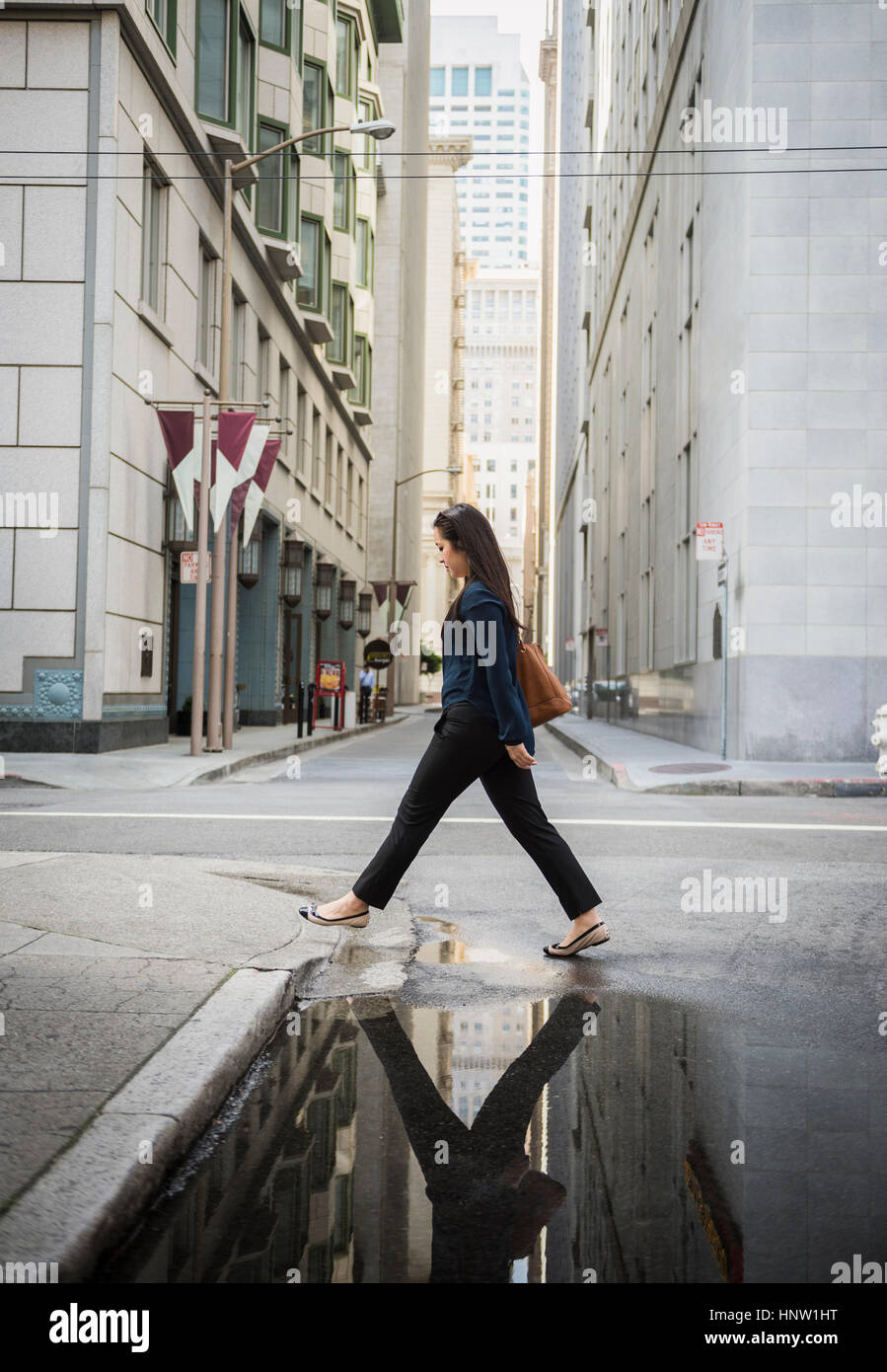Reflet dans puddle of Chinese businesswoman crossing street Banque D'Images