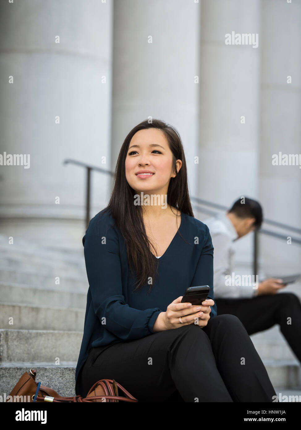 Chinese businesswoman sitting on staircase holding cell phone Banque D'Images