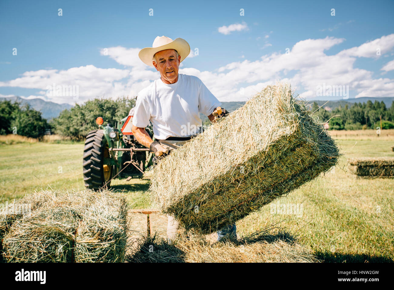 Caucasian farmer in field levée bale of hay Banque D'Images