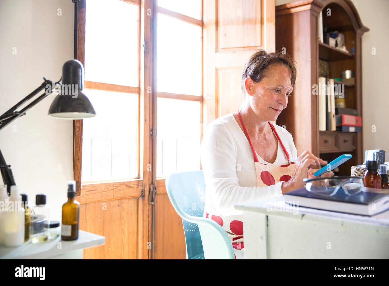 Mature Woman texting on smartphone bureau dans l'atelier du savon fait à la main Banque D'Images