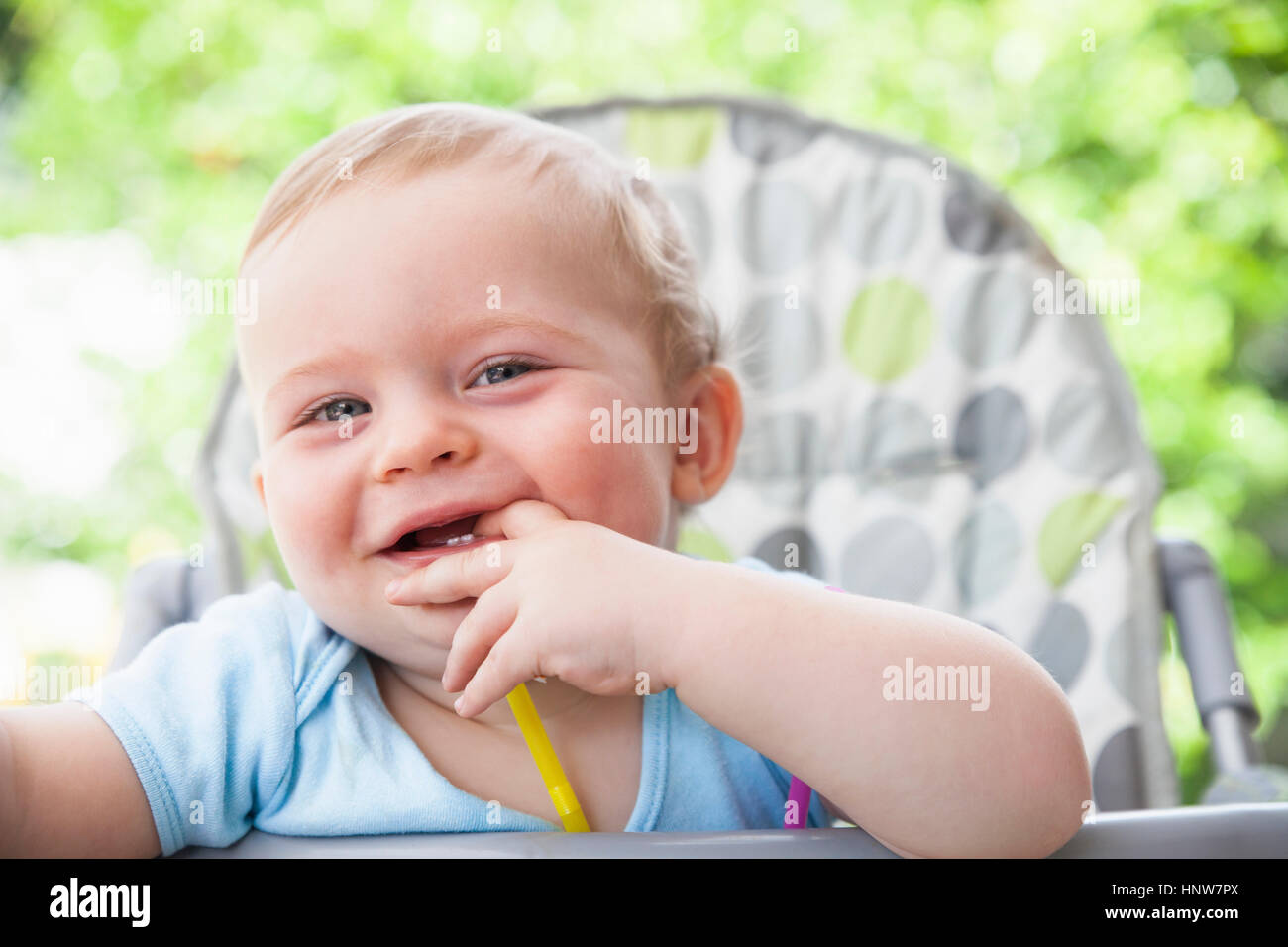 Portrait of Baby Boy avec les doigts dans la bouche sur la chaise haute en jardin Banque D'Images