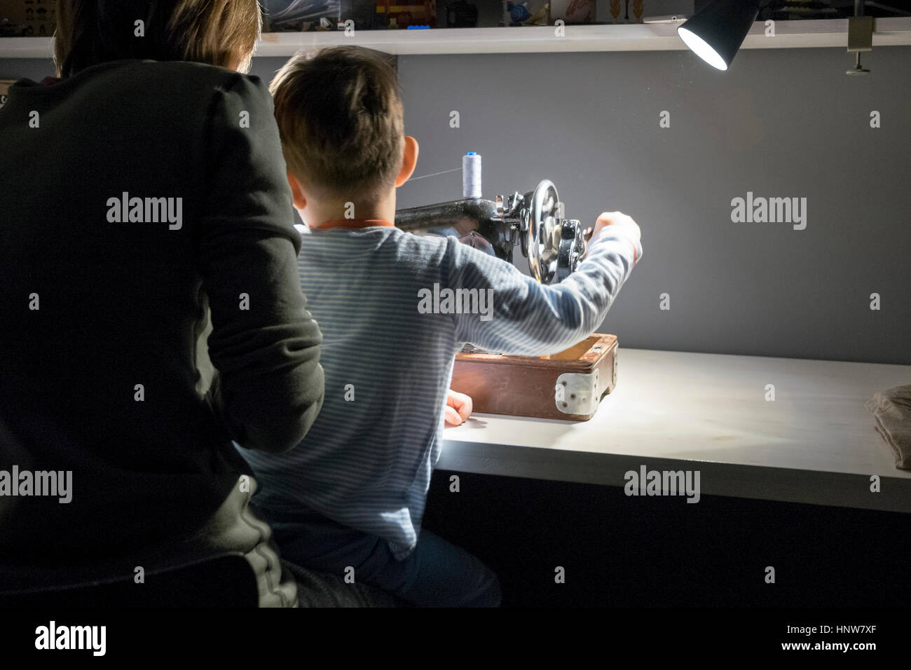 Vue arrière du garçon avec mère apprendre à tourner la poignée de la machine à coudre Banque D'Images