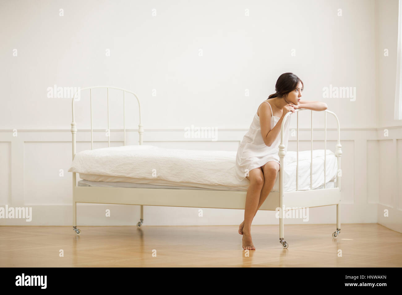 Jeune femme sombre sitting on bed Banque D'Images