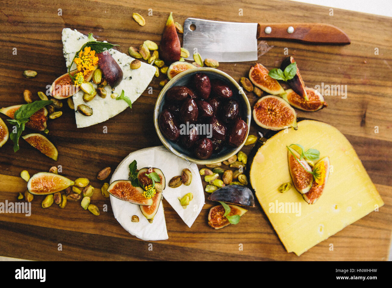 Plateau de fromages divers avec des figues, olives, pistaches, planche à découper en bois sur cleaver Banque D'Images