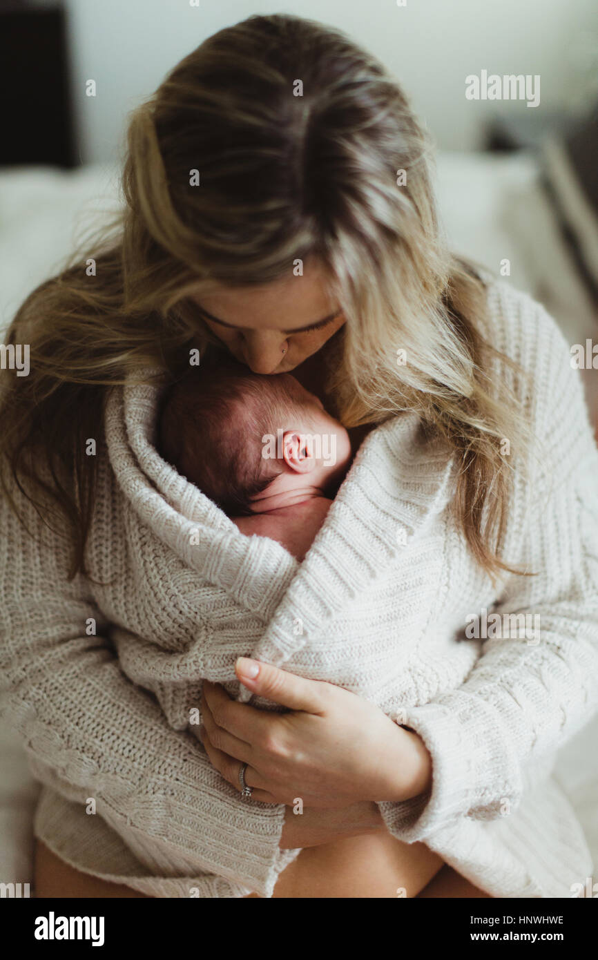Mid adult woman kissing bébé nouveau-né fille enveloppé à Cardigan Banque D'Images