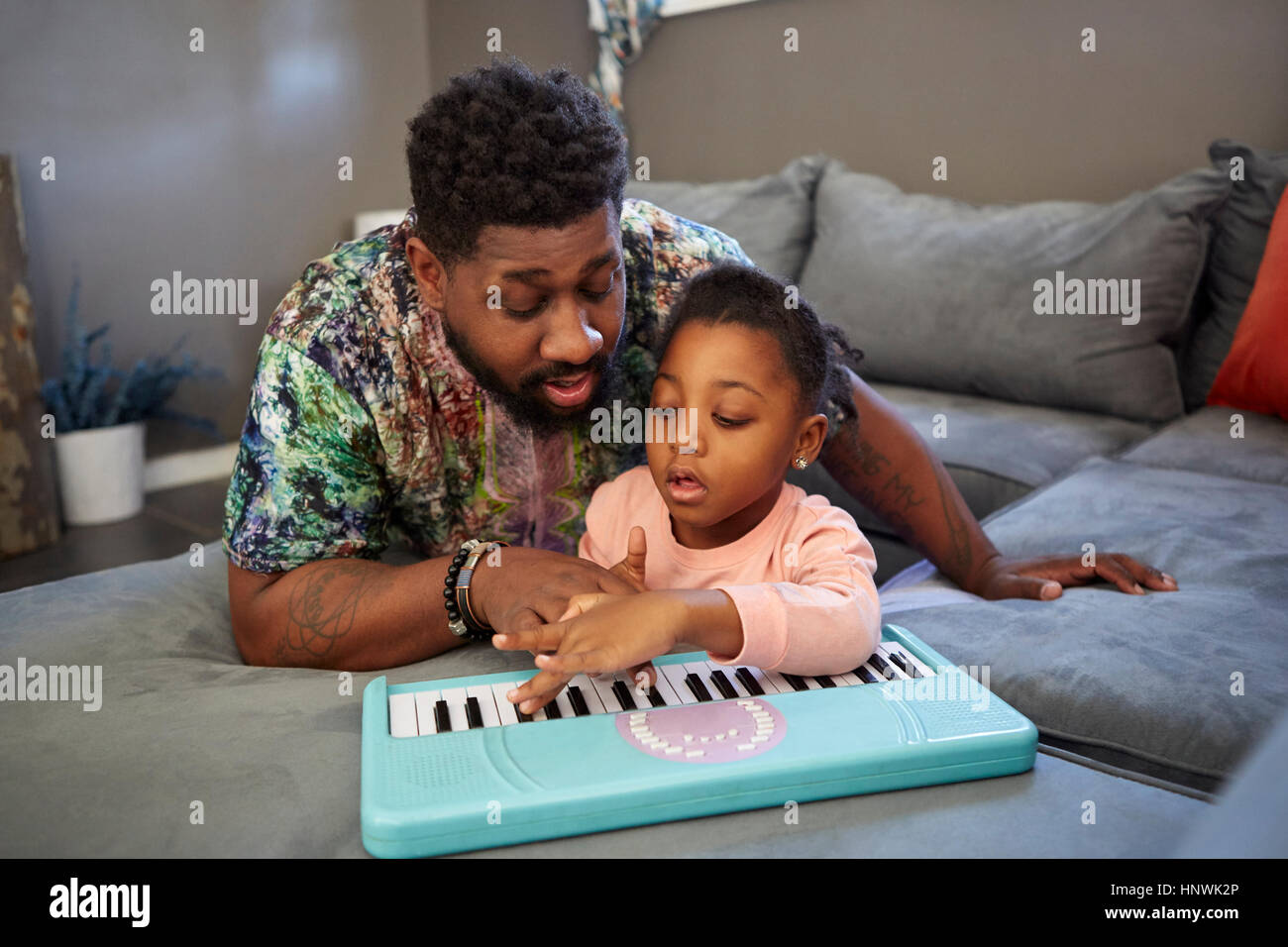 Girl lying on sofa avec père jouant clavier jouet Banque D'Images