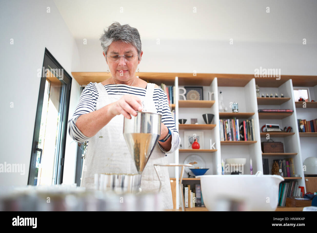 Senior woman in kitchen, à l'aide de l'entonnoir de crêpes de se passer de la crème, des cosmétiques, dans des pots, mid section Banque D'Images