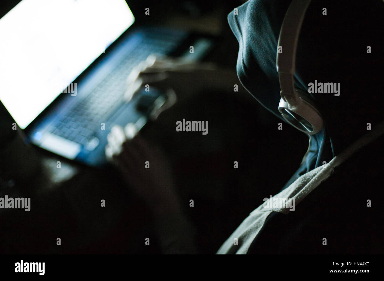 Homme hacker dans le capot et écouteurs working on laptop in the dark Banque D'Images