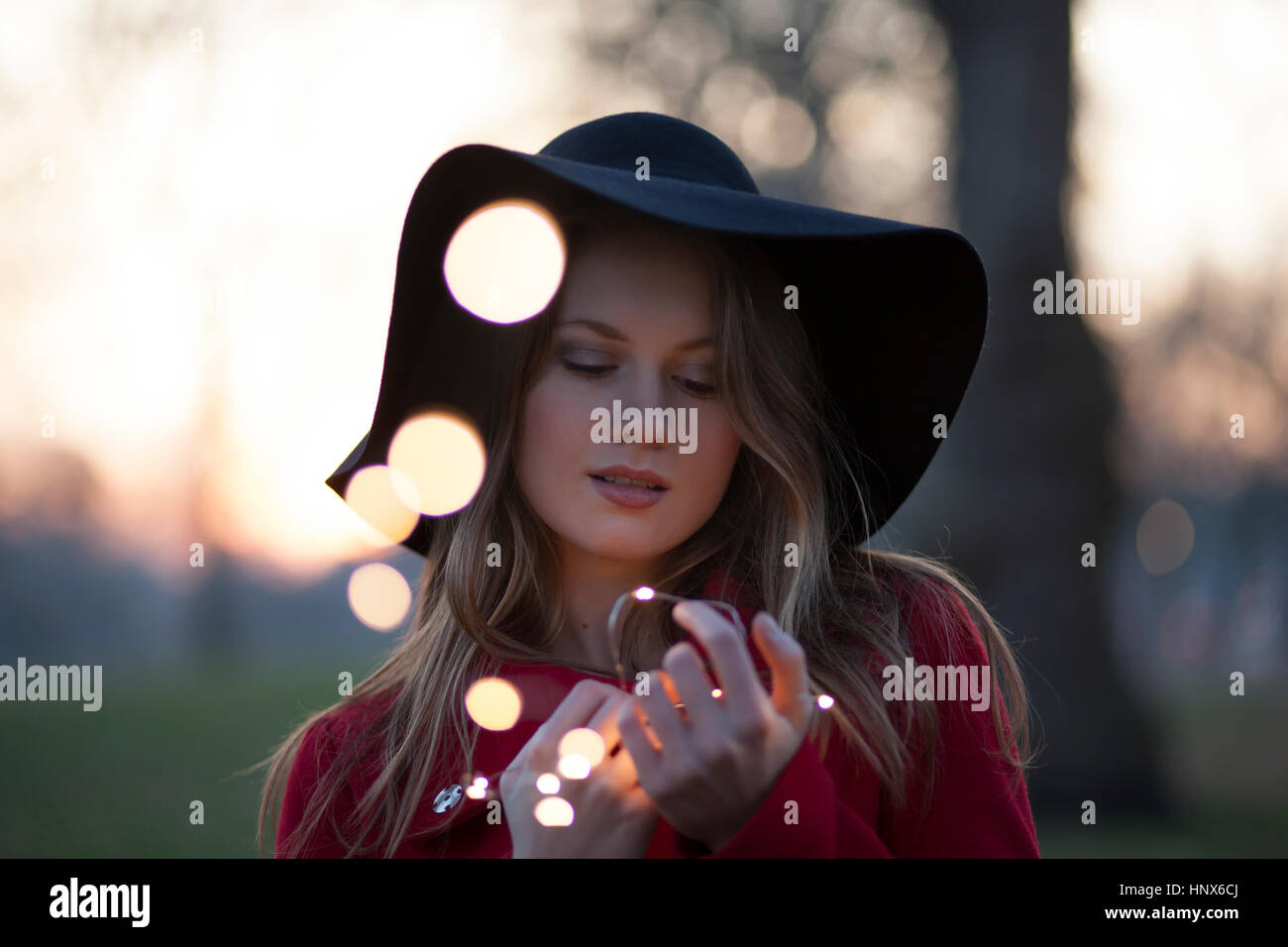 Jeune femme dans le parc à la recherche de lumières dans sa main, London, UK Banque D'Images