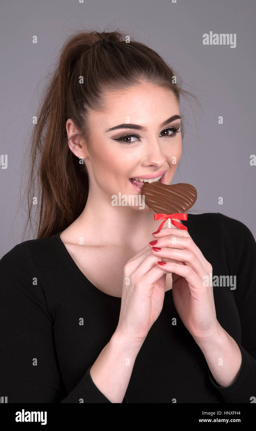 Portrait of a young woman eating a chocolat coeur sur un bâton Banque D'Images