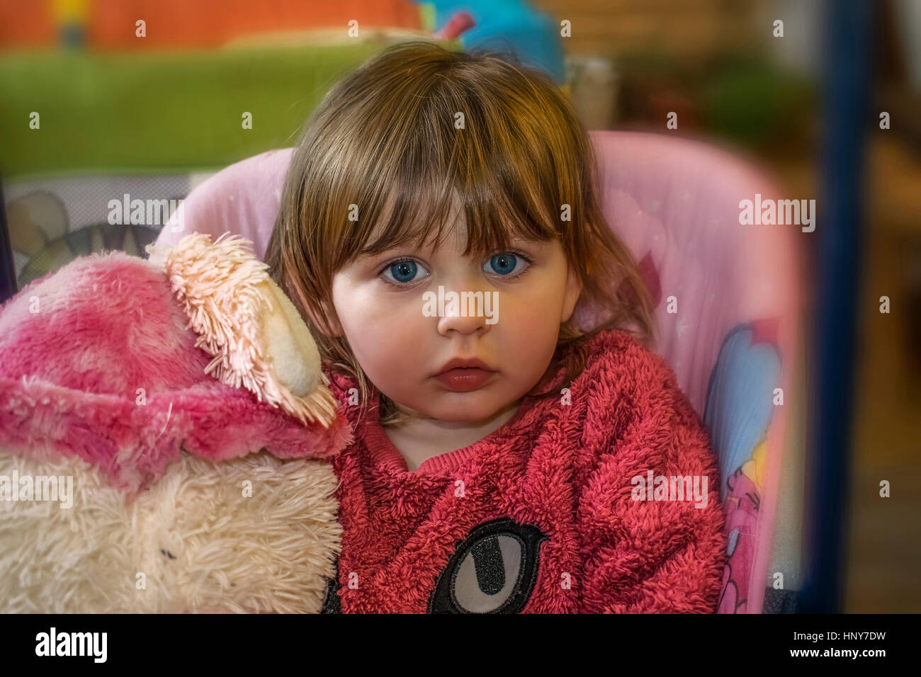 Petite fille blonde avec des yeux bleus portant un chandail rose à fourrure, innocemment dans l'appareil photo et la tenue d'un ours en peluche. Banque D'Images