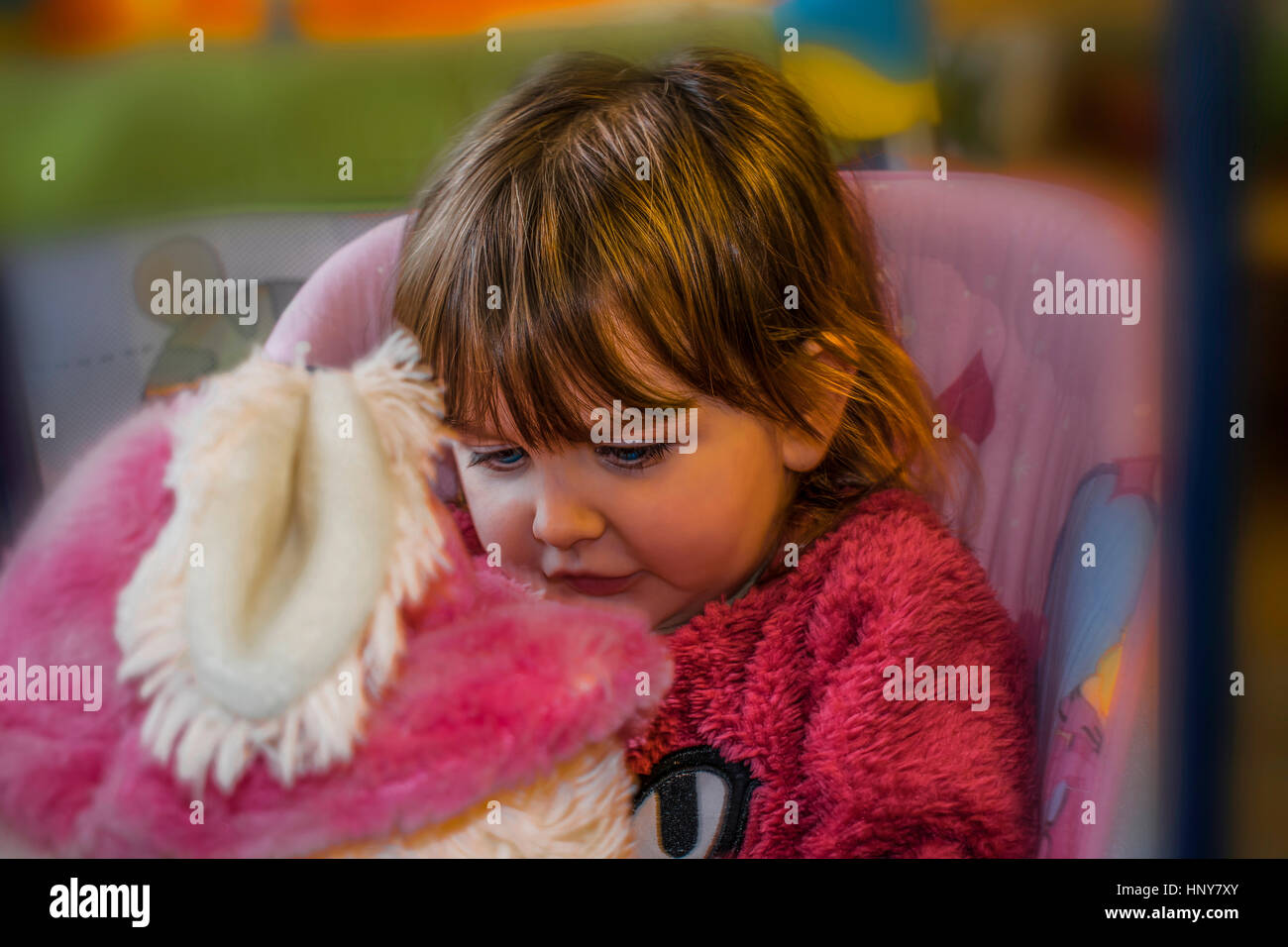 Petite fille blonde avec des yeux bleus, assis sur une balançoire, vêtu d'un chandail de laine fourrure et la regarder bêtement le furry ours. Banque D'Images