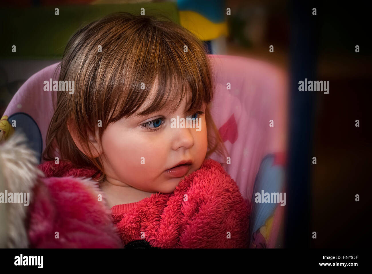 Petite fille blonde avec des yeux bleus dans un pull en fourrure rose assis sur une balançoire et à la recherche sur le côté. Banque D'Images