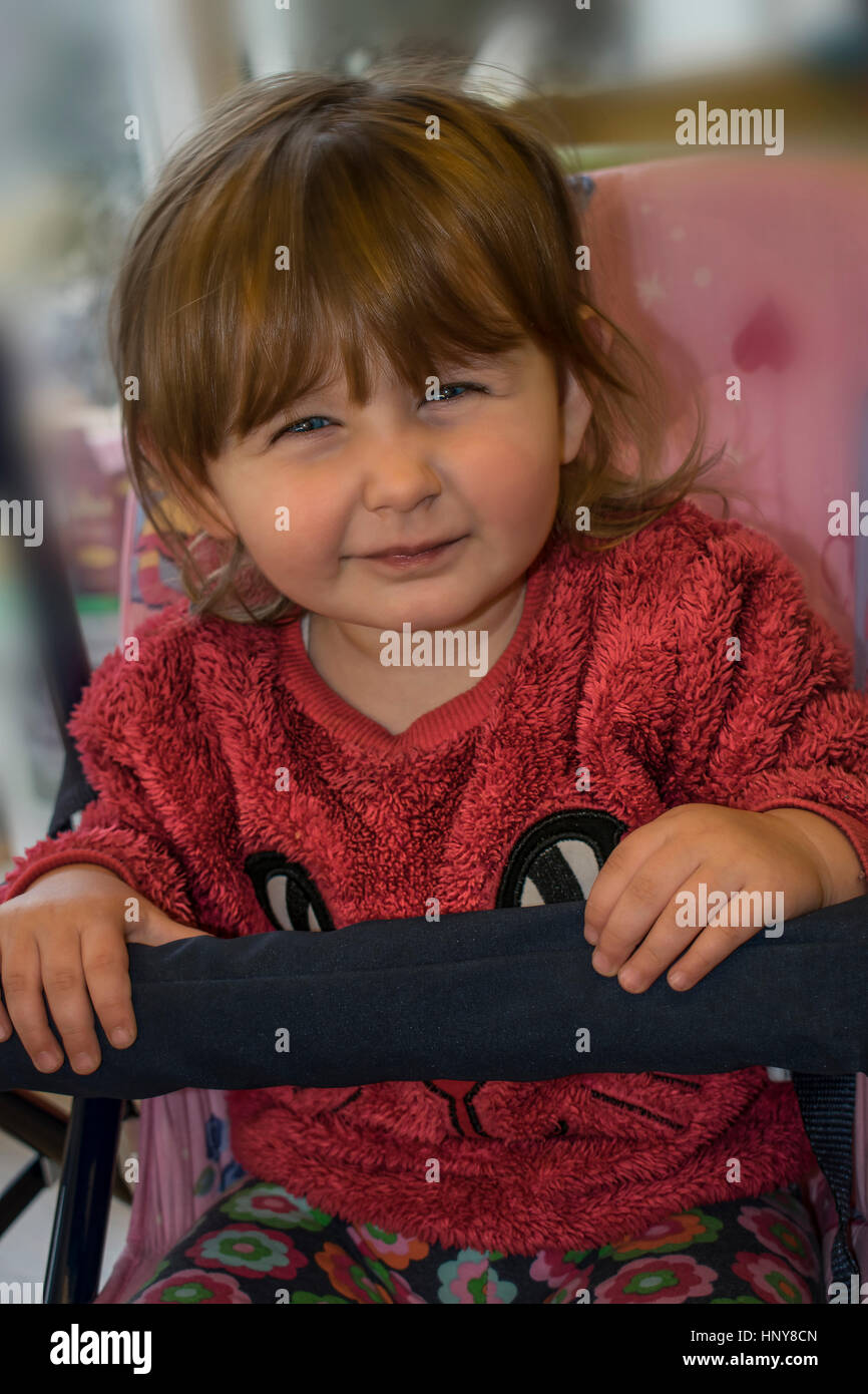 Petite fille blonde assise sur une balançoire et portant un chandail de fourrure rose, tout en faisant une grimace à la caméra. Banque D'Images
