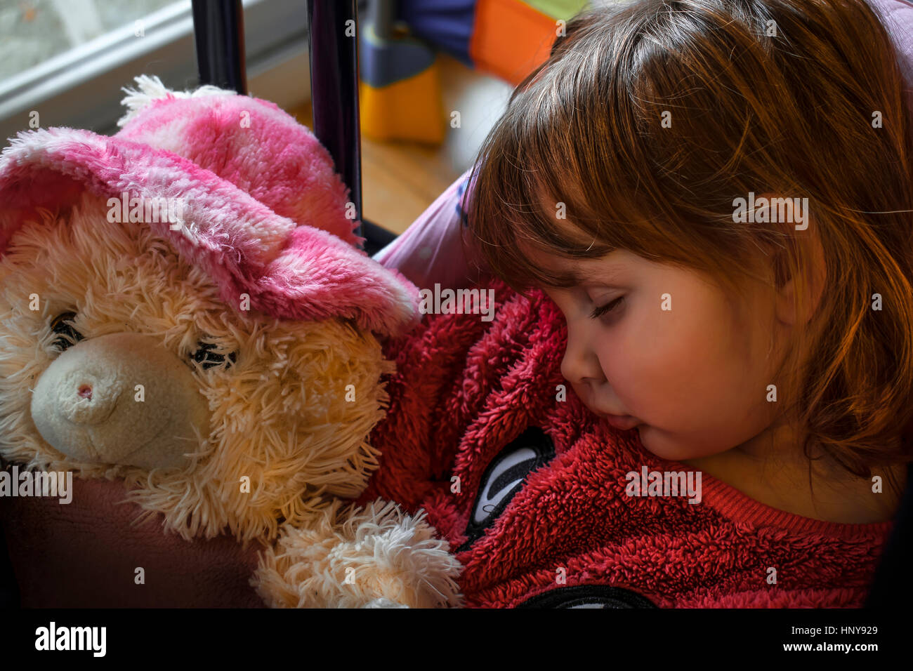 Petite fille blonde portant un chandail de fourrure rose endormie avec un ours en peluche dans ses mains. Banque D'Images