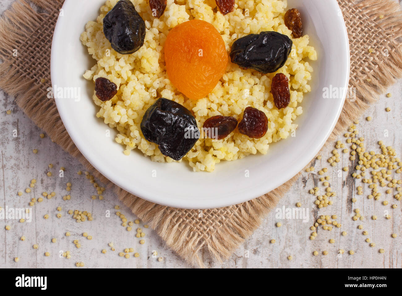 Gruau de millet cuit avec des raisins secs, d'abricot séché et de prune sur plaque blanche, concept d'une saine alimentation, nutrition et petit déjeuner nutritif Banque D'Images