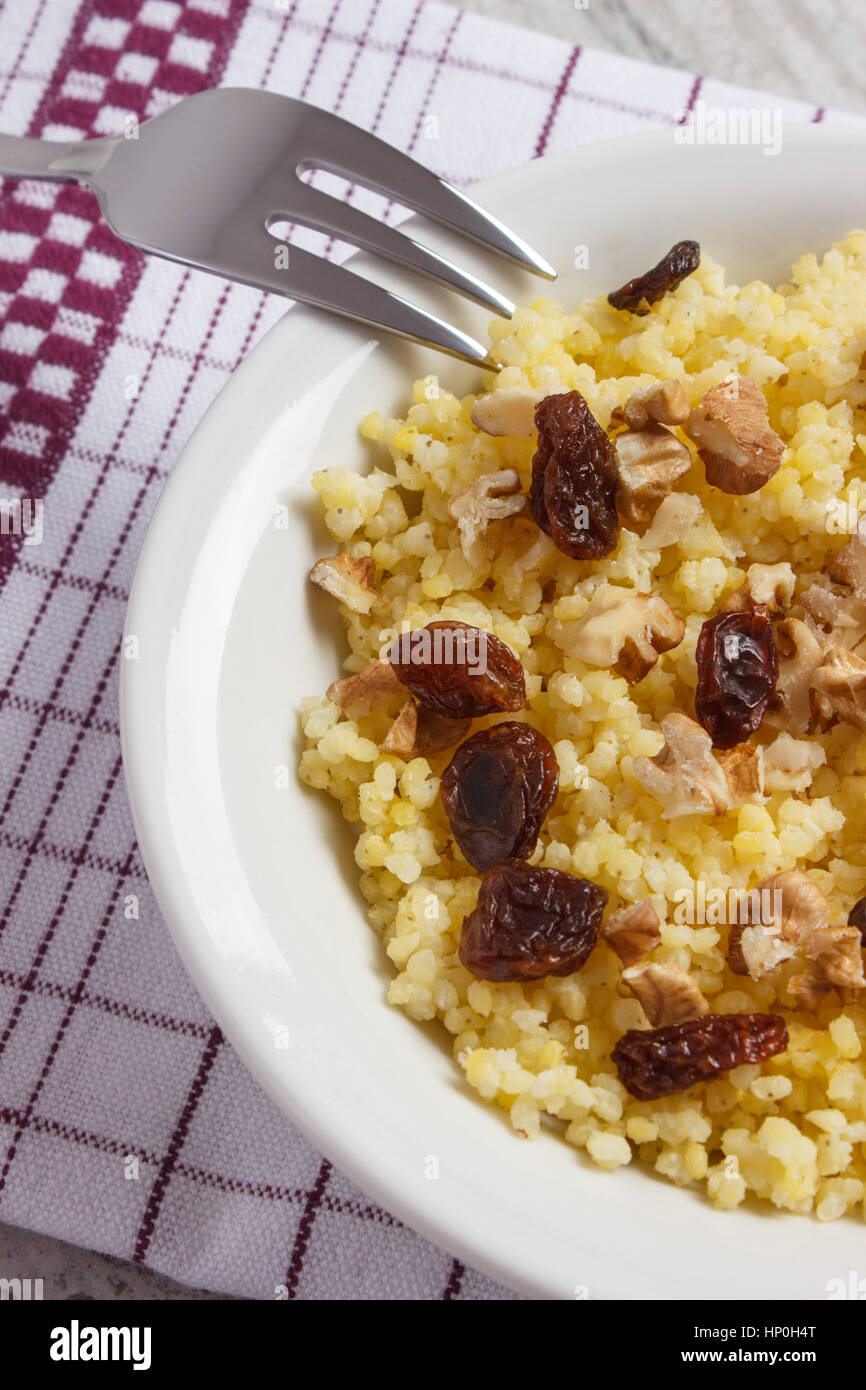 Gruau de millet cuit avec des raisins secs et les noix sur la plaque blanche, concept d'une saine alimentation, nutrition et petit déjeuner nutritif Banque D'Images