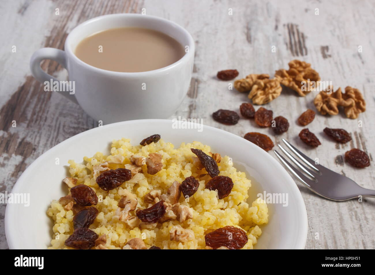 Gruau de millet cuit avec des raisins secs et les noix sur la plaque blanche, tasse de café avec du lait, du concept de la saine alimentation, nutrition et petit déjeuner nutritif Banque D'Images