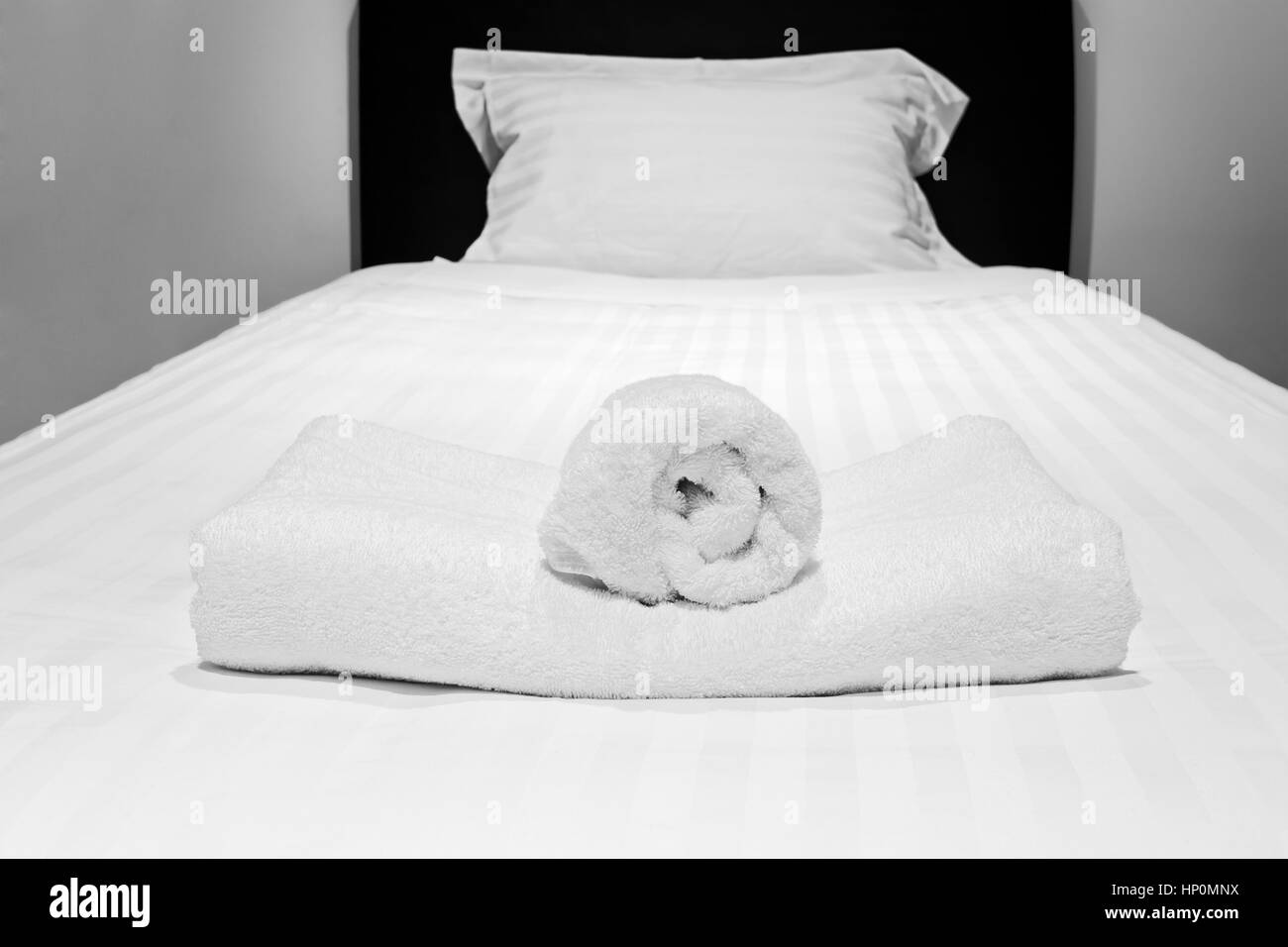 Seul lit préparé avec des draps blancs et des serviettes roulées en attente pour les clients en hébergement de luxe chambre à coucher. Banque D'Images