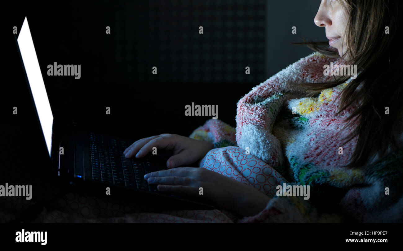 Beautiful smiling woman restent au lit tenir la main sur le clavier de l'ordinateur portable et le type. Regarder les actualités, pour les examens de lecture, réseau social, internet chat su Banque D'Images