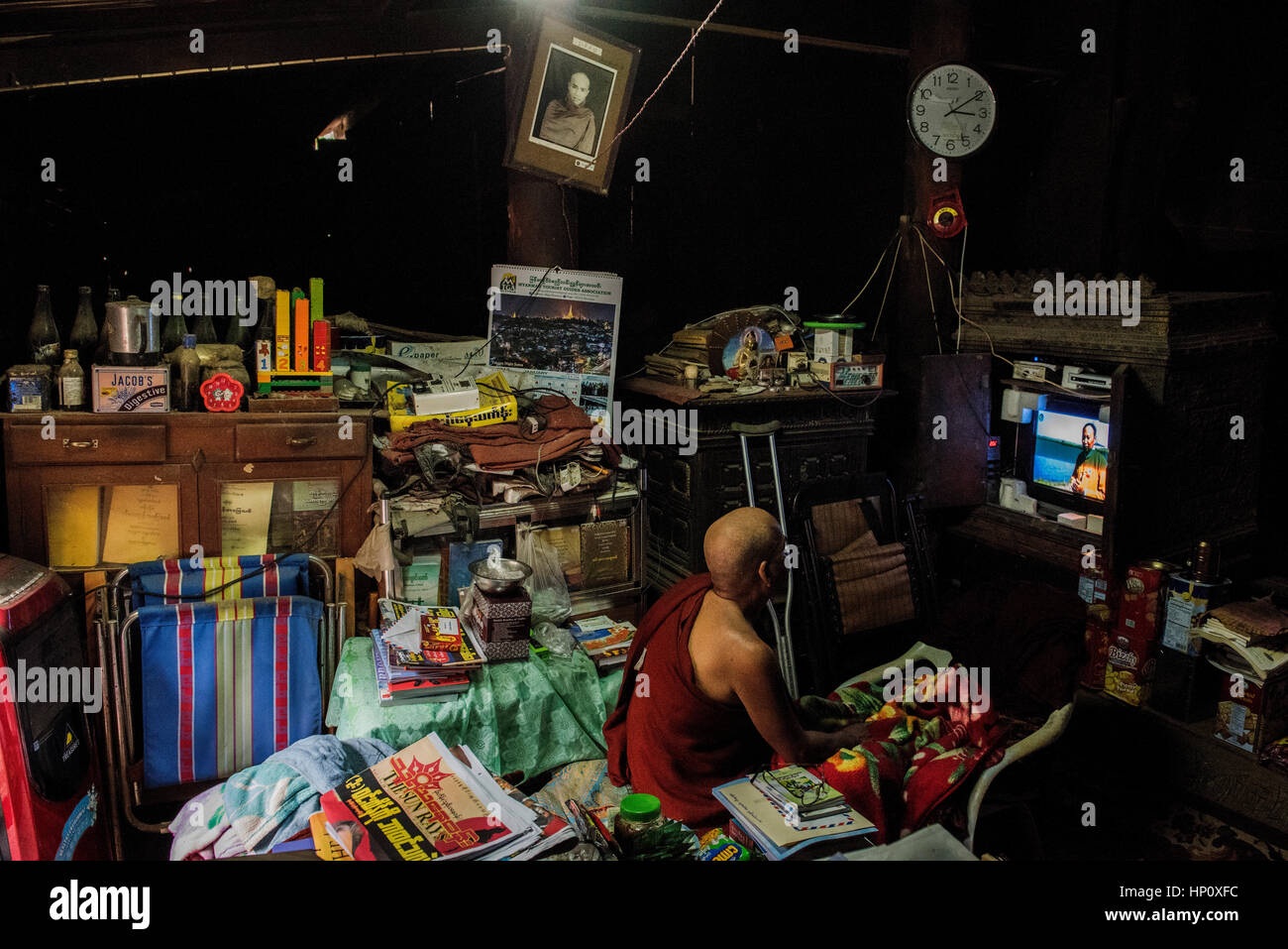 Un moine bouddhiste est assis à regarder la télévision entouré par ses effets personnels dans une partie de l'Bagaya Monastey Ava dans une ancienne capitale de la Birmanie Banque D'Images