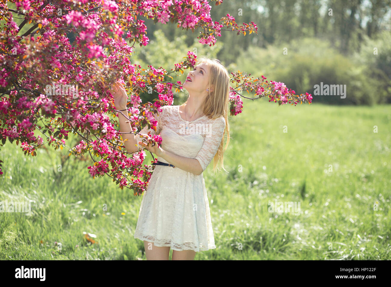 Belle jeune fille en robe blanche bénéficiant au parc pendant la saison des cerisiers en fleur sur un beau printemps Banque D'Images