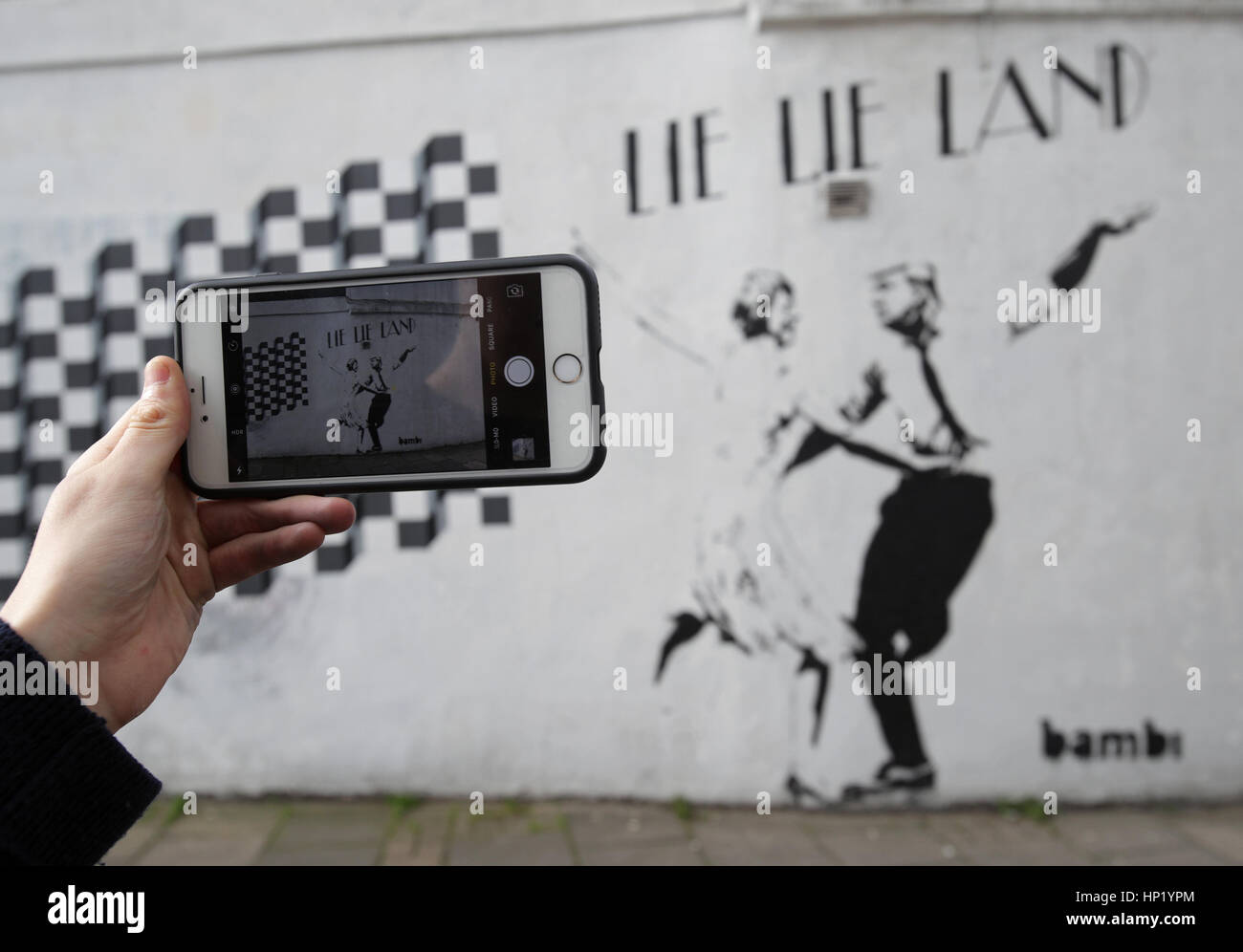 Un homme prend une photo d'un morceau de l'art de rue par l'artiste Bambi, intitulé mentir mentir Land - représentant le premier ministre Theresa mai et le président américain, Donald Trump, dansant dans une pose parodiant le film La La Land - à Islington, Londres. Banque D'Images