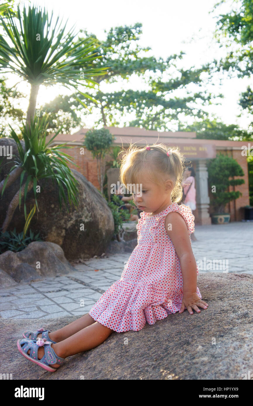 Belle petite fille est assise sur un rocher sur le coucher du soleil. Ponagar tours. Vietnam Banque D'Images