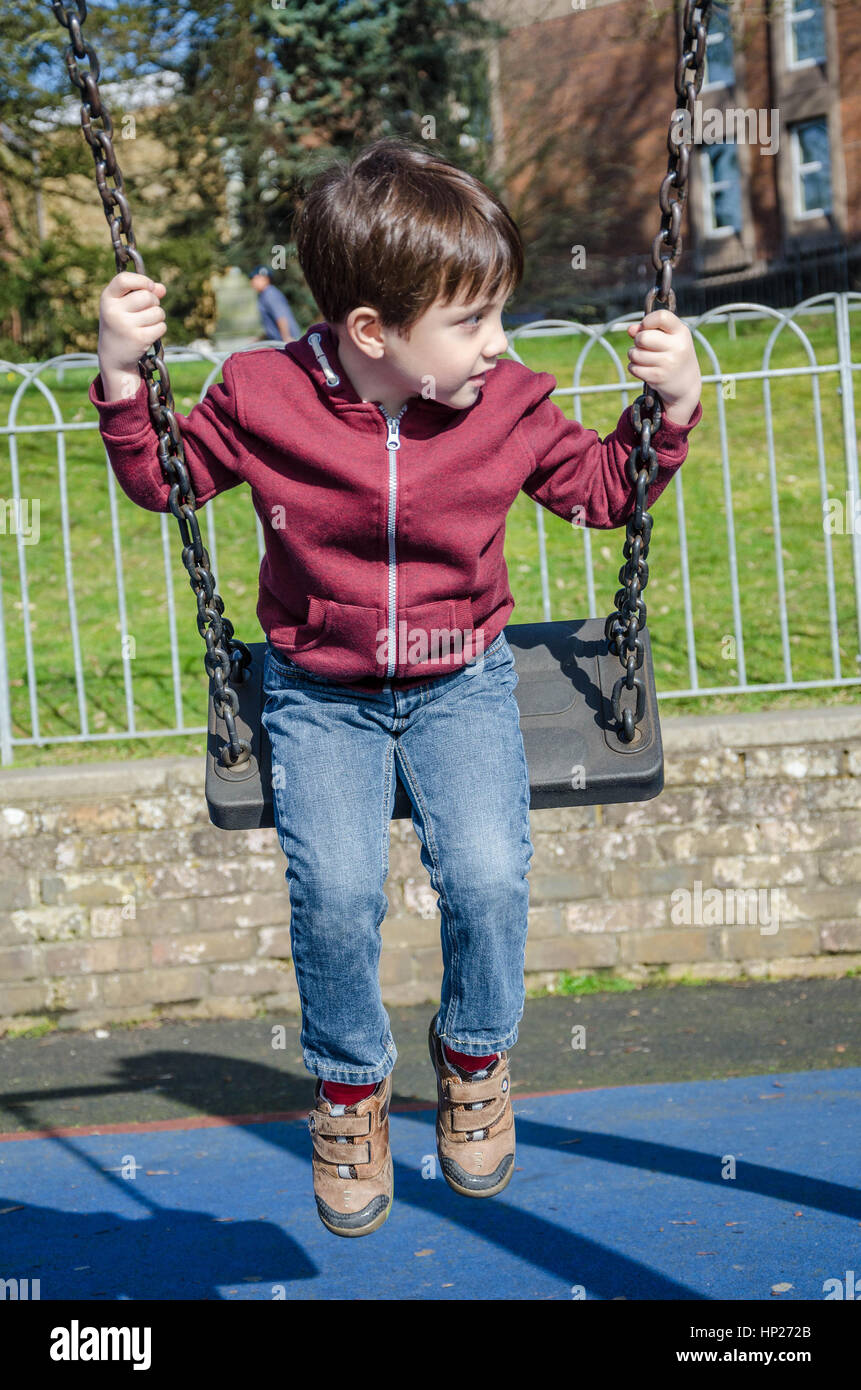 Un jeune garçon joue sur une balançoire dans un aire de jeux pour enfants. Banque D'Images