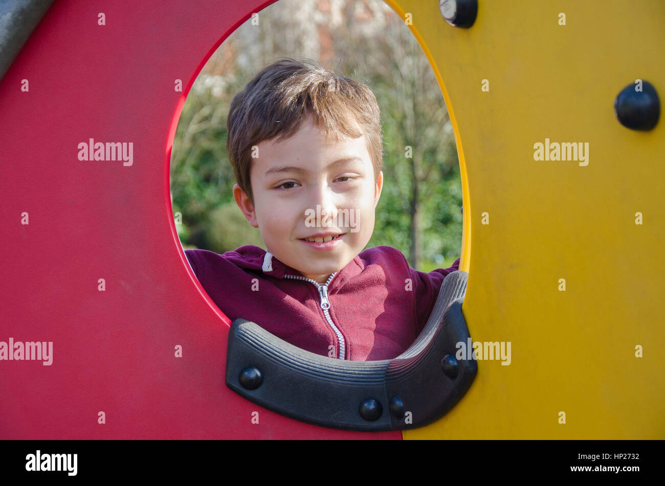 Un jeune garçon pose pour une photo à travers un hublot dans une escalade dans une aire de jeux pour enfants. Banque D'Images