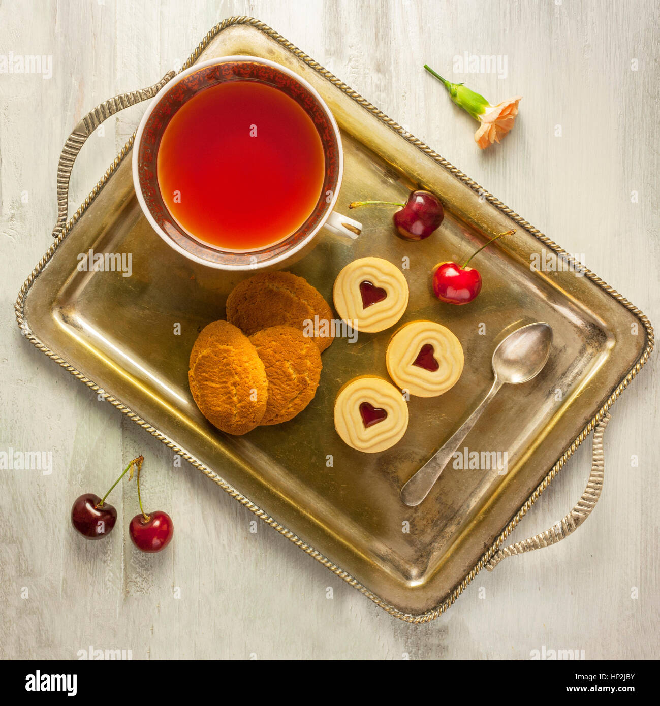 Une photo d'un plateau vintage avec une tasse de thé, des biscuits, et des cerises, tourné à partir de ci-dessus, sur un parquet en bois clair texture conseils Banque D'Images