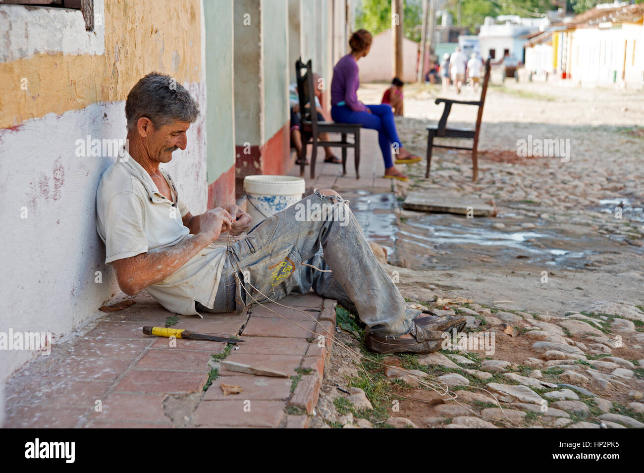 Un homme assis sur le trottoir à l'ombre de sa chambre travaillant sur des cordages à Trinidad Cuba Banque D'Images
