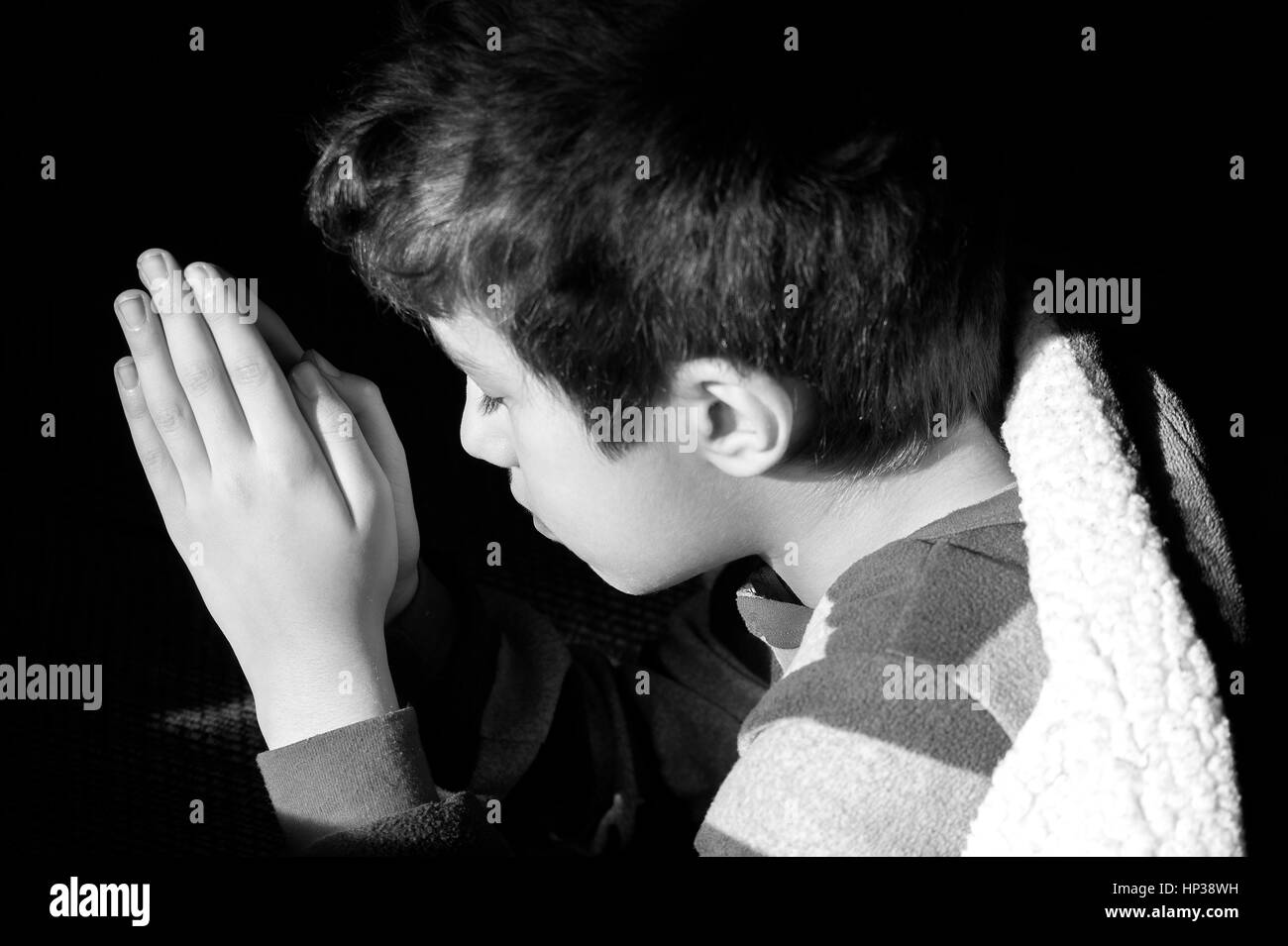 Jeune garçon à genoux pour prier à l'heure du coucher, les yeux clos, photo de foi chrétienne, concept religieux Banque D'Images