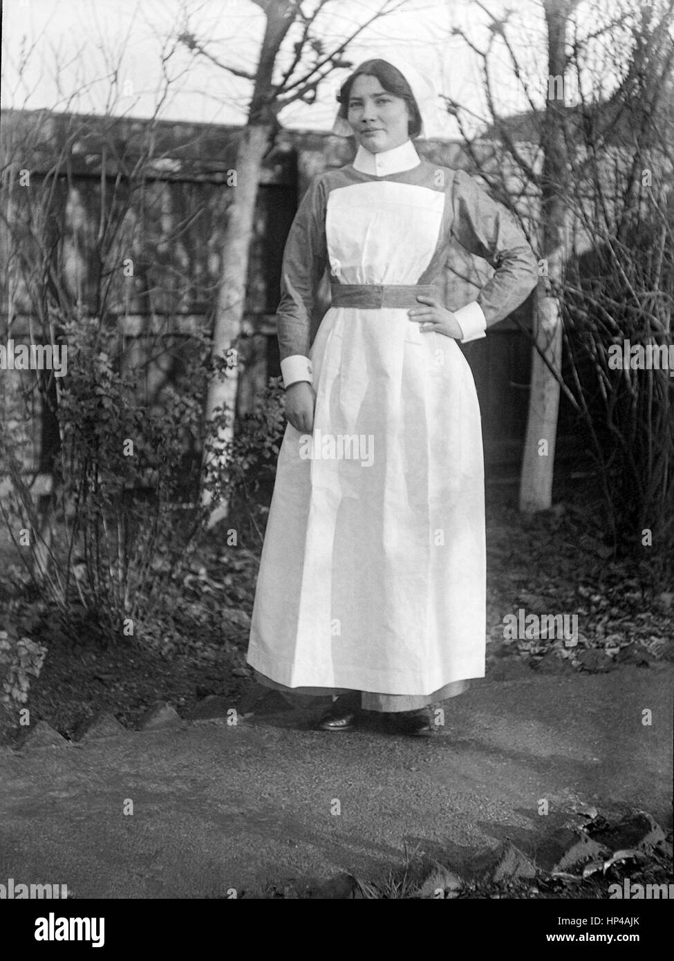 Une jeune dame debout édouardienne sur un chemin près d'une clôture en bois dans un jardin arrière. Elle porte un uniforme de nouvelles infirmières, peut-être St Johns Ambulance Brigade, sans insigne..restauré à partir d'une numérisation haute résolution prises à partir de l'original Edwardian négatif. Image prise vers 1910 Banque D'Images