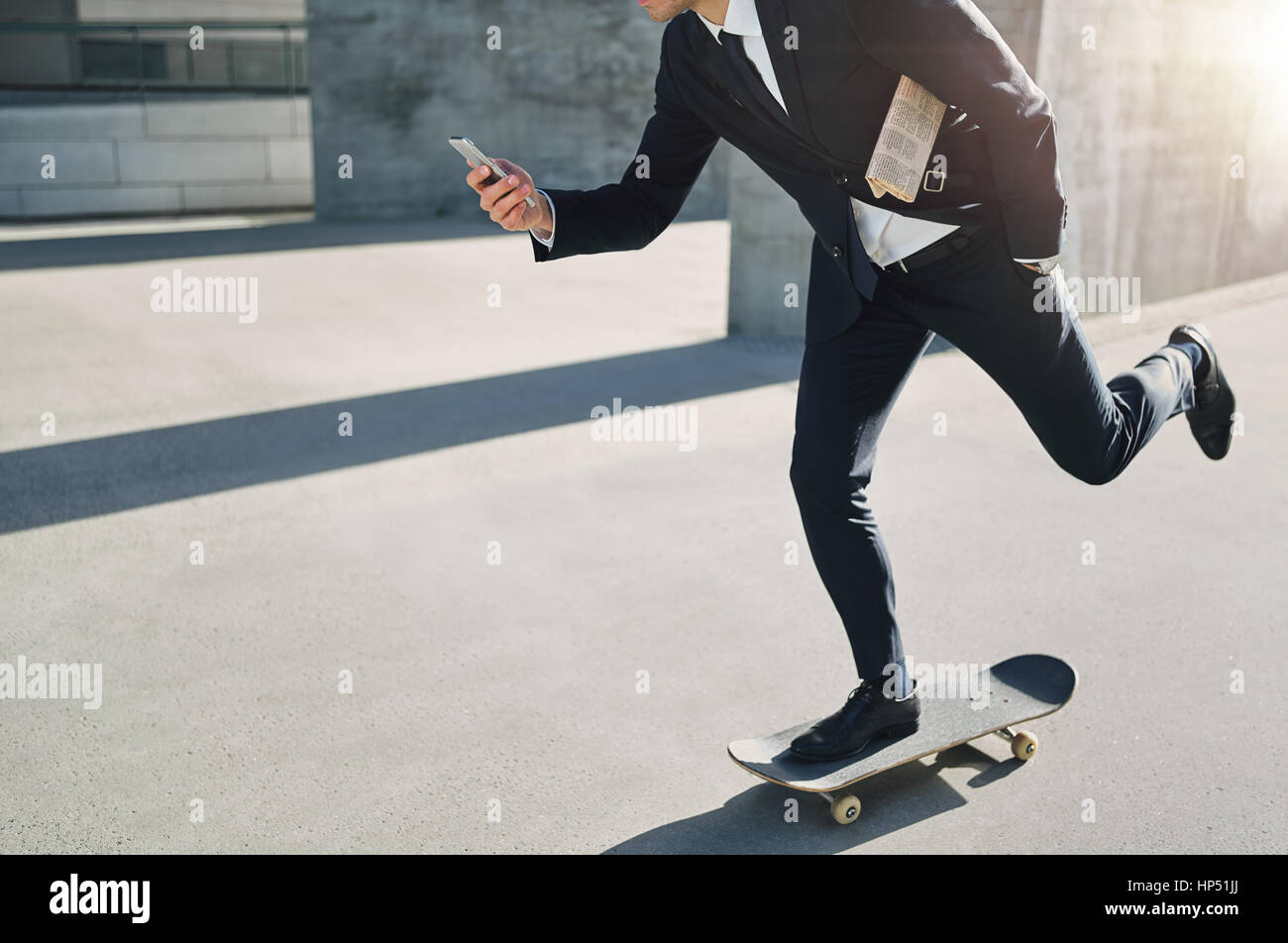 Vue de face d'un homme d'affaires sur un skateboard en regardant son téléphone en déménagement Banque D'Images