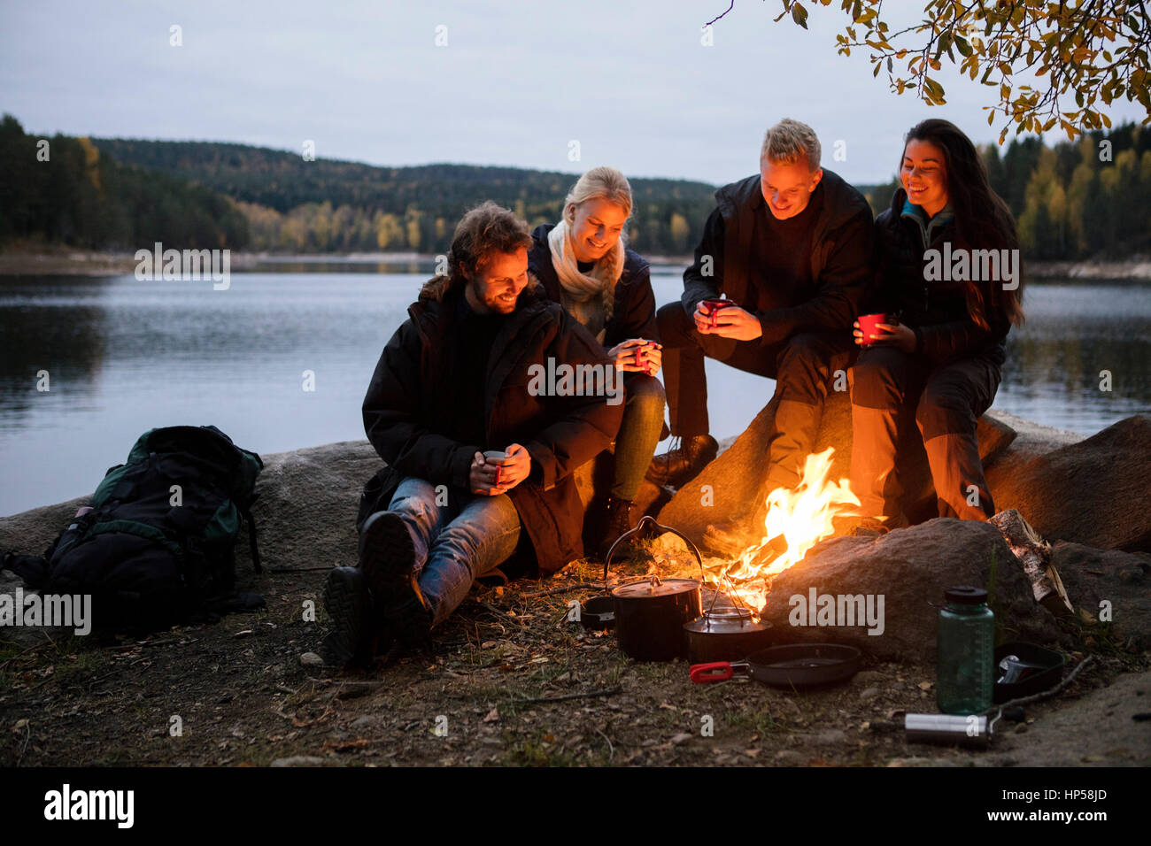 Amis avec les tasses de café assis au feu de camp sur Lakeshore Banque D'Images