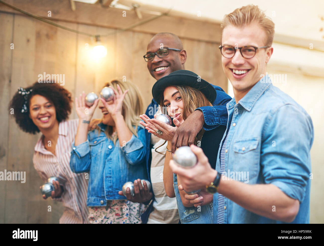 Group of smiling beaux jeunes hommes et femmes dans des vêtements à l'intérieur permanent et posant à huis clos tenue pétanque boules de métal, rire Banque D'Images
