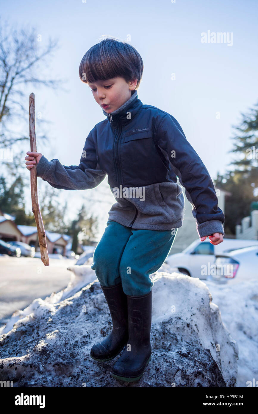 Garçon avec stick jouant sur neige. Banque D'Images