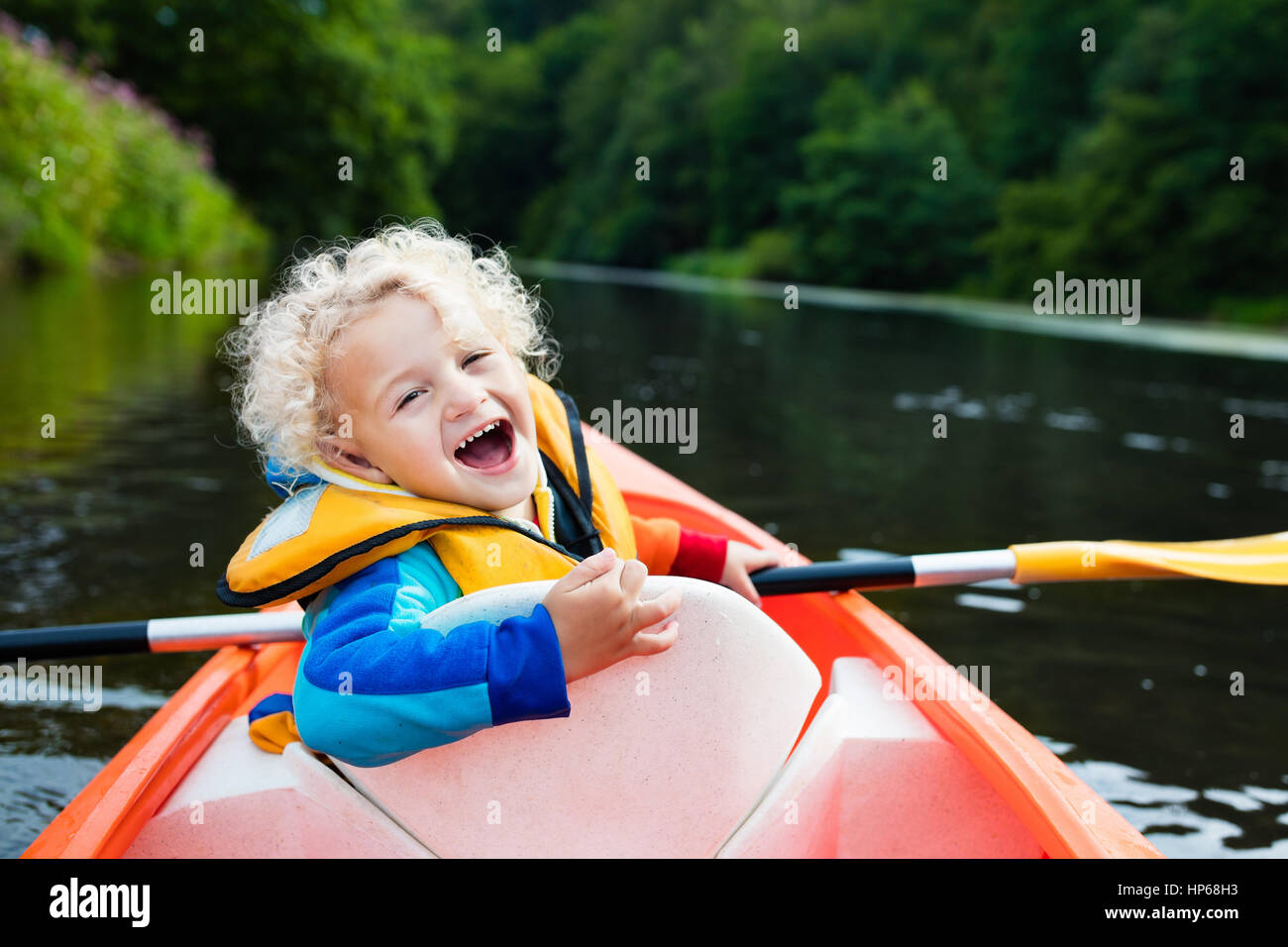 Happy kid bénéficiant en kayak sur la belle rivière. Peu curly bébé garçon  kayak sur chaude journée d'été. Sport d'eau et de camping de plaisir. Canoe  pour les enfants Photo Stock -